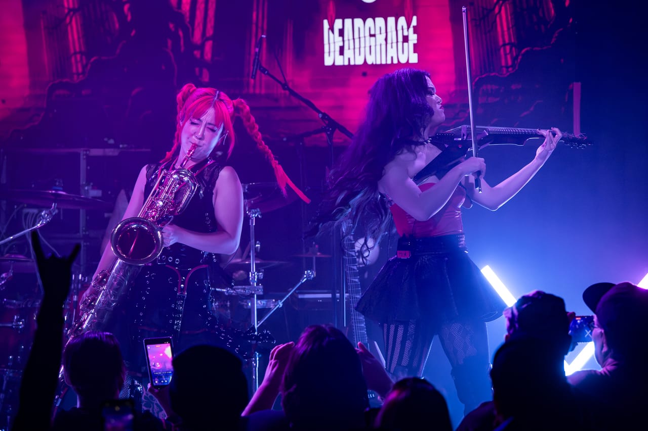 Grace Kelly on saxophone and Mia Asano on violin play side by side under purple light in Albuquerque, hands raised in the crowd in front of them