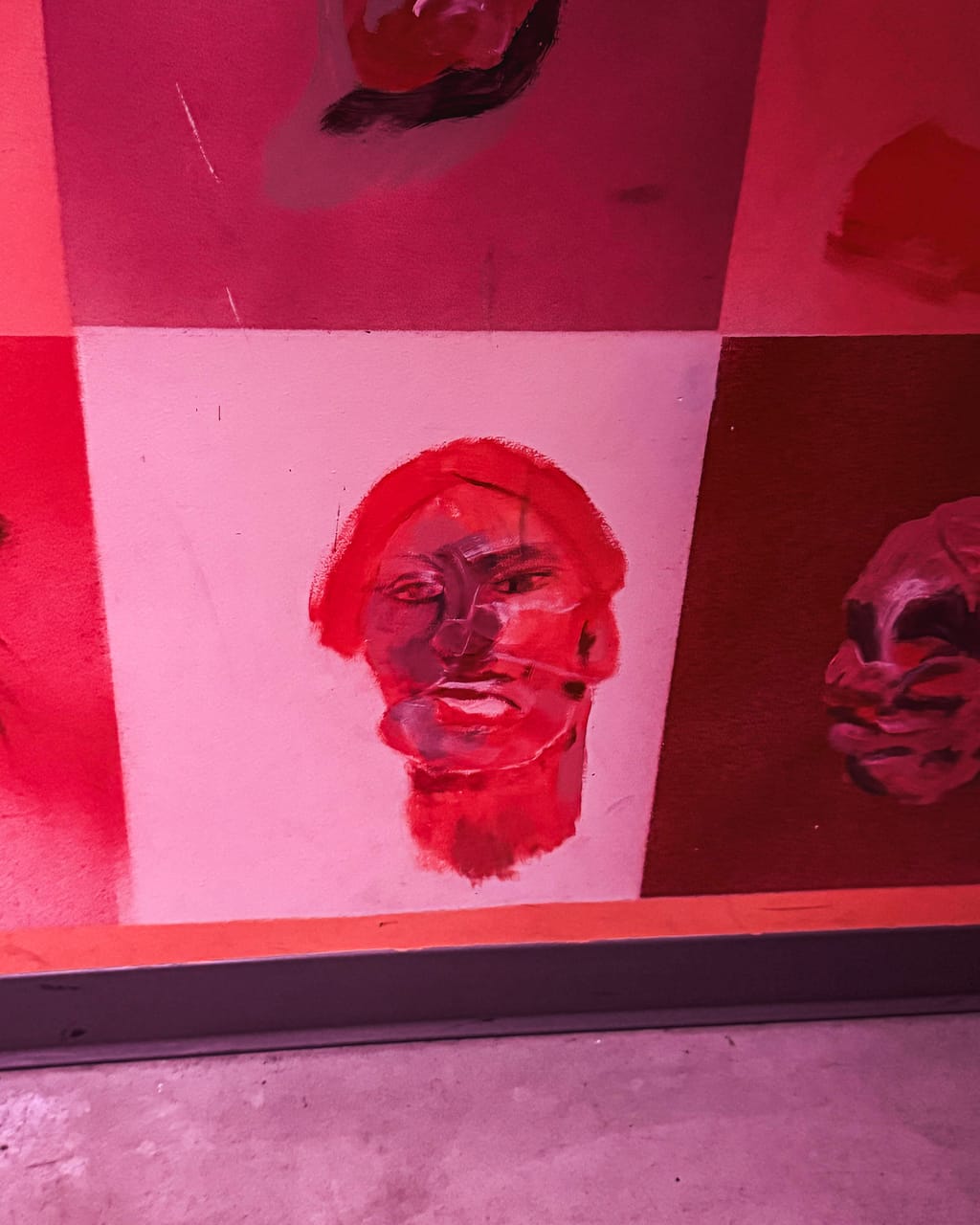 Painted face portraits in red and pink covering the walls of a room at Meow Wolf, Denver