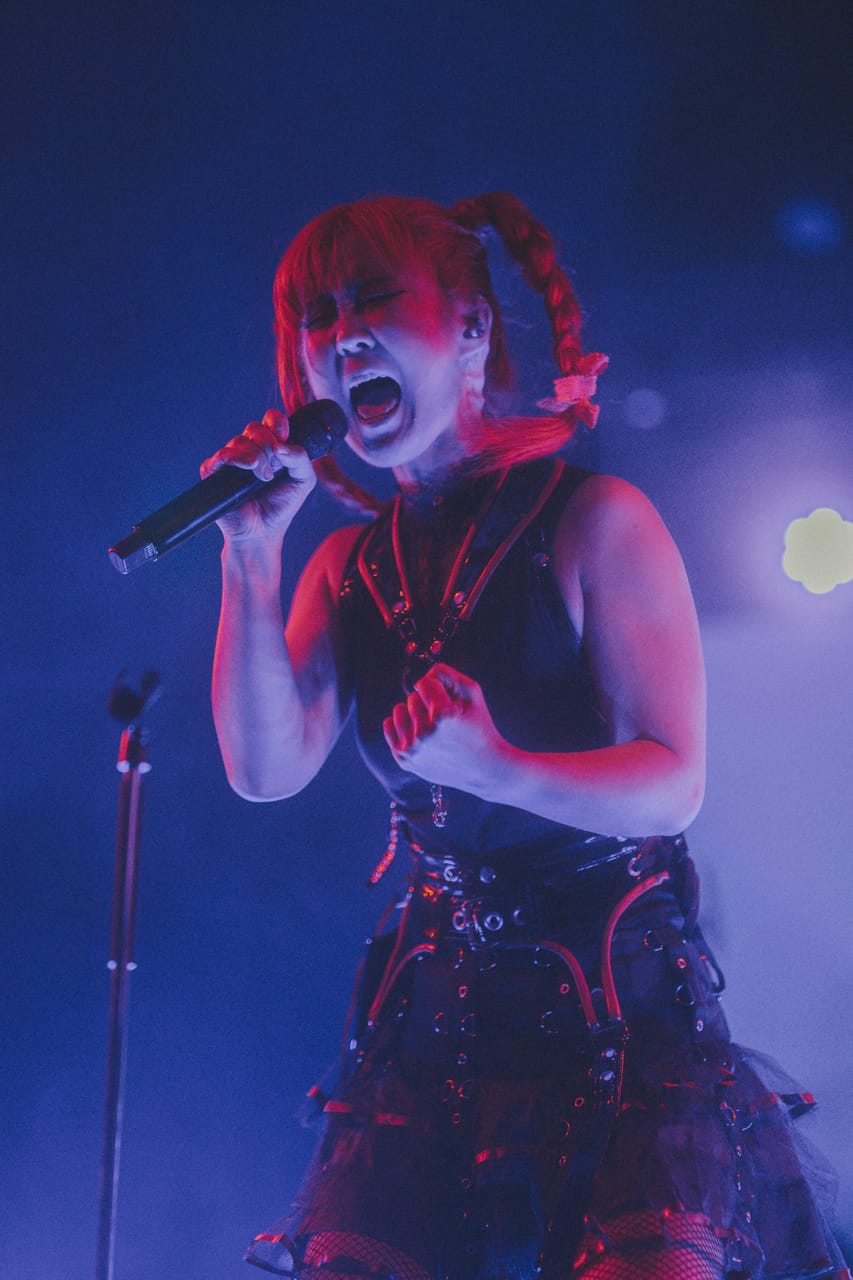 Grace Kelly of DEADGRACE screams into a handheld microphone, fist clenched, under blue and red light at the Star Theater, Portland