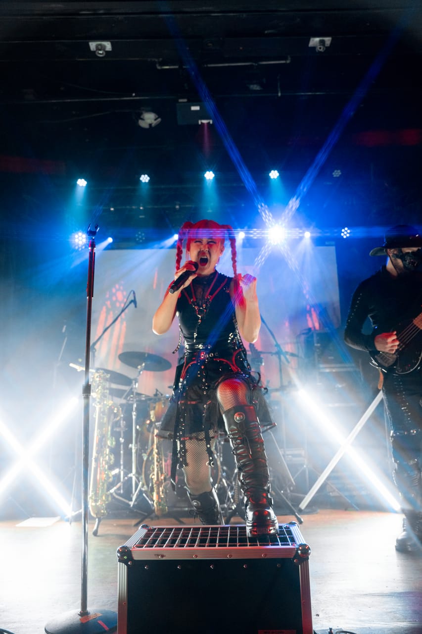Grace Kelly of DEADGRACE stands on a road case and screams into a microphone under white and blue stage lights at the Star Theater, Hampus Isaksson on bass at the edge of the frame