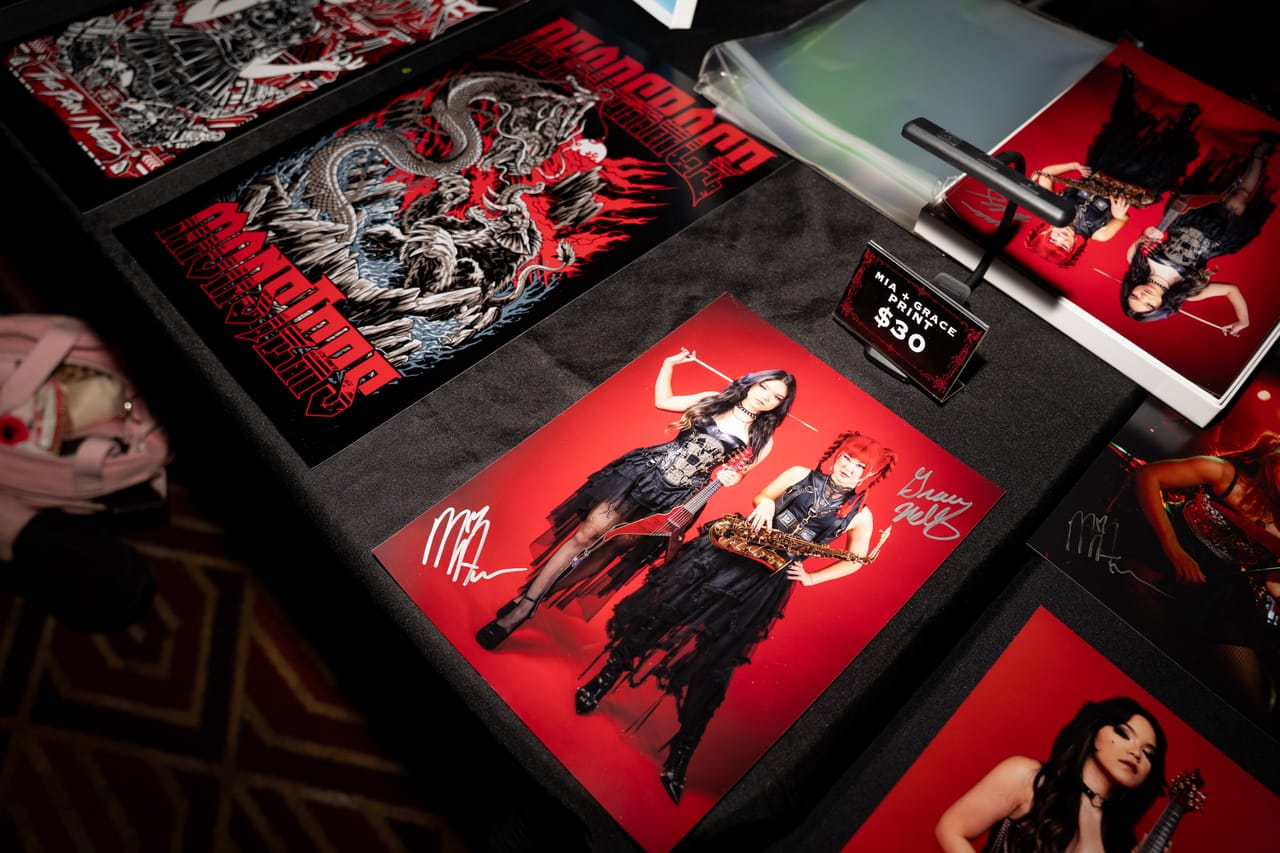 Close-up of the DEADGRACE merch table: posters and a signed Mia & Grace print priced at $30