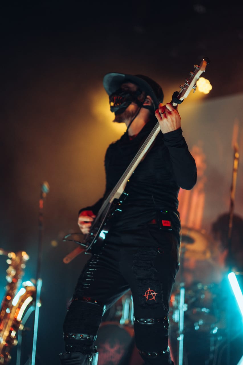 DEADGRACE bassist Hampus Isaksson, in a black hat and fanged mask, plays bass in warm stage light at the Star Theater, Portland