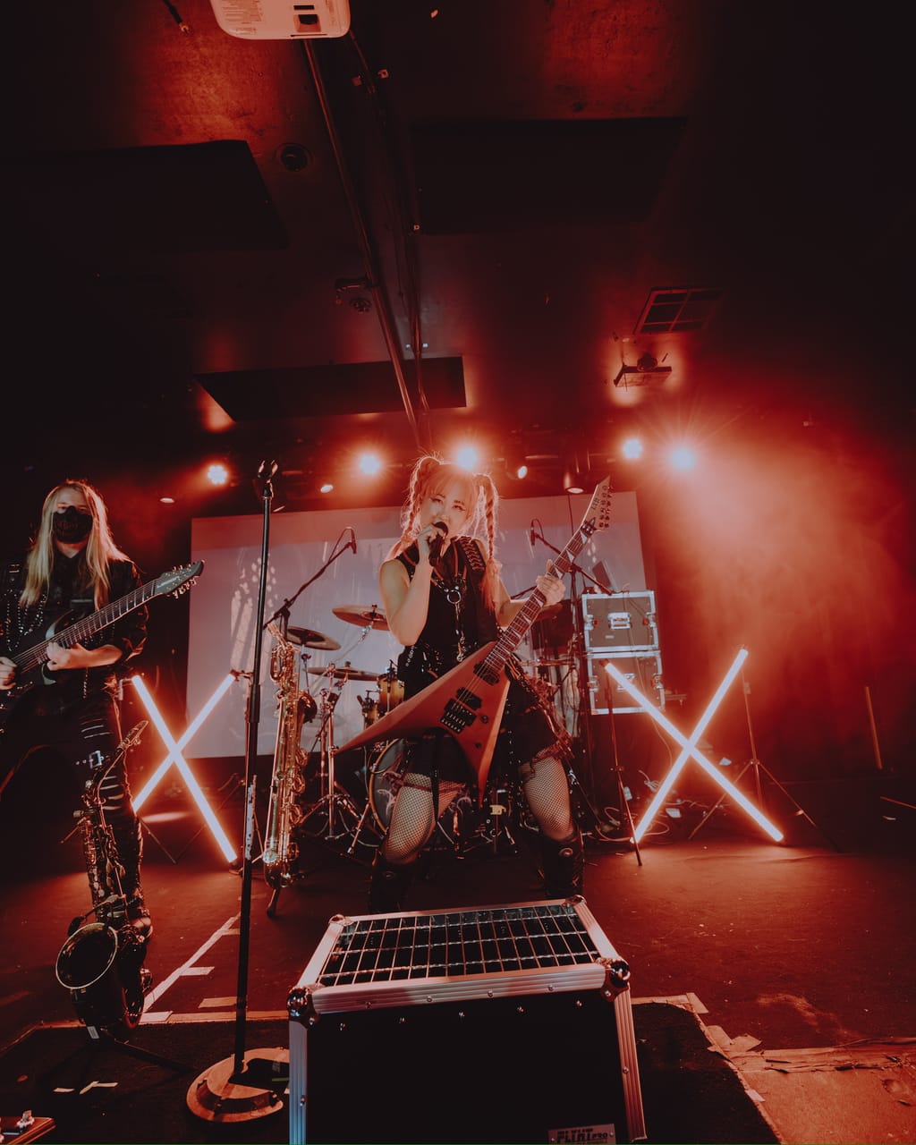 DEADGRACE on stage at Harlow's: Grace Kelly sings while playing a red flying-V guitar between two neon X lights, masked guitarist Sam Fairless plays stage left, saxophones on stands