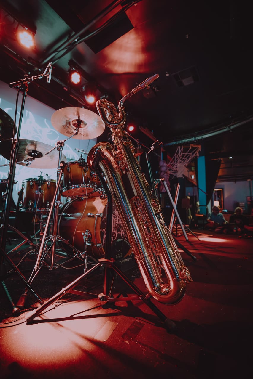 Grace Kelly's baritone saxophone on its stand in front of the DEADGRACE drum kit under red lights on the stage at Harlow's in Sacramento, before the set