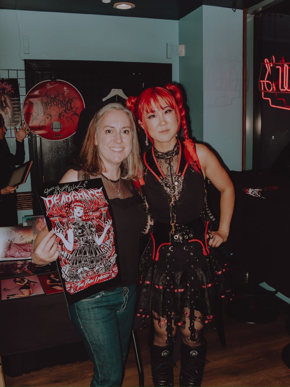 Grace Kelly at Harlow's with a fan holding a signed DEADGRACE "The Pain I Need" poster, a Mia Asano CD hanging on the wall behind them