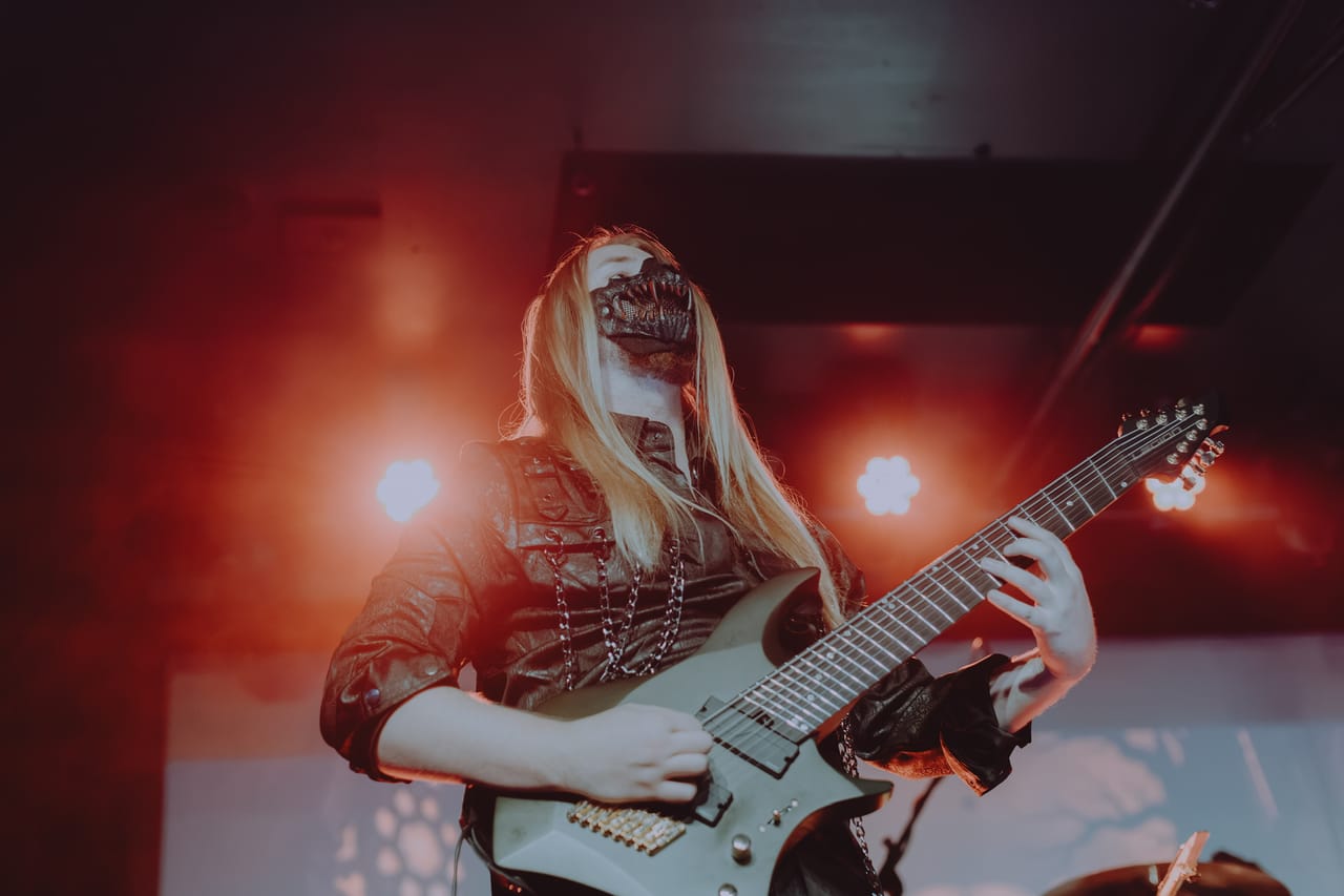 DEADGRACE guitarist Sam Fairless, long blond hair and a black skull-style mask, plays an 8-string guitar under red lights at Harlow's in Sacramento