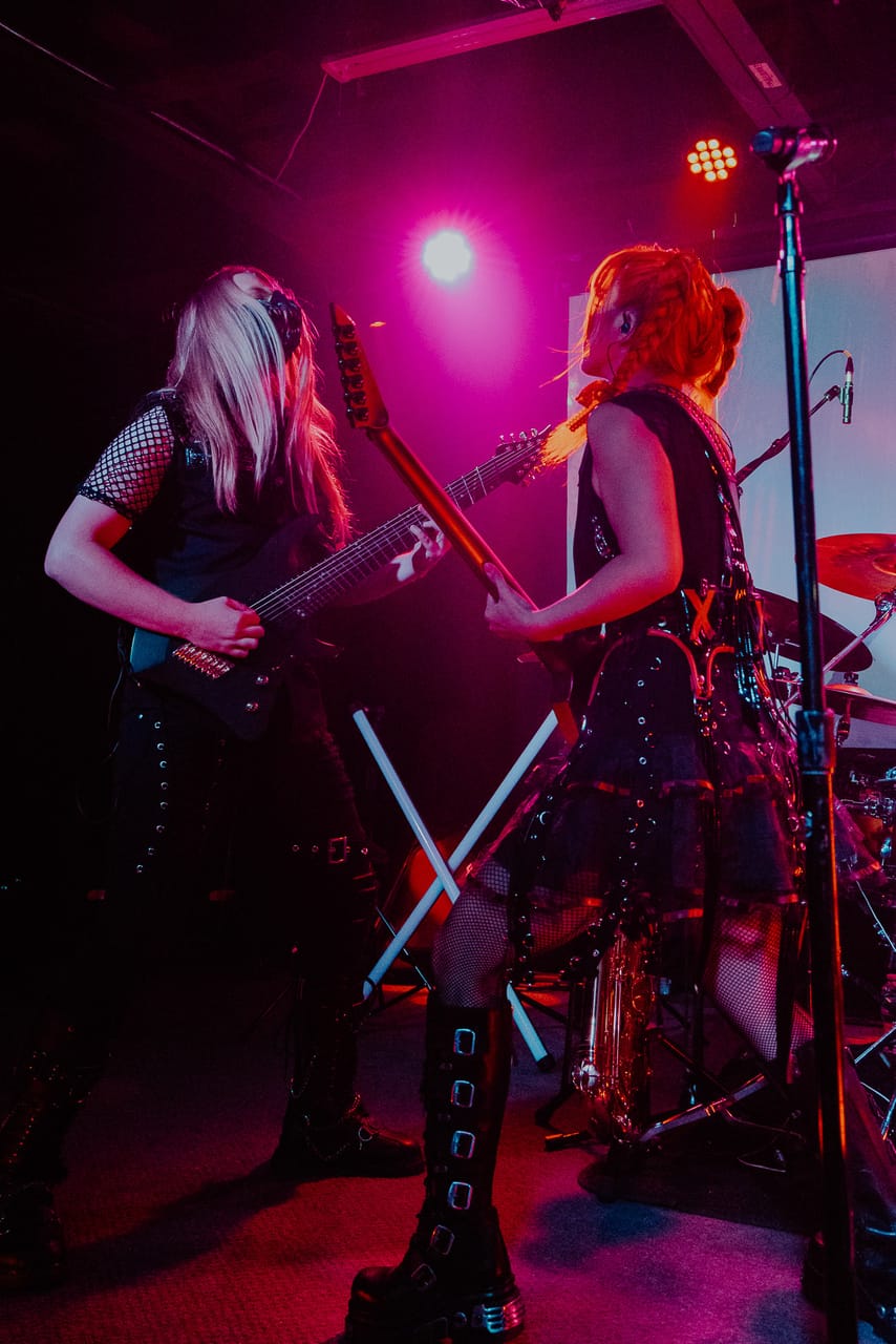 Sam Fairless and Grace Kelly play guitars side by side under pink light at the Urban Lounge, Salt Lake City, crossed light bars behind them