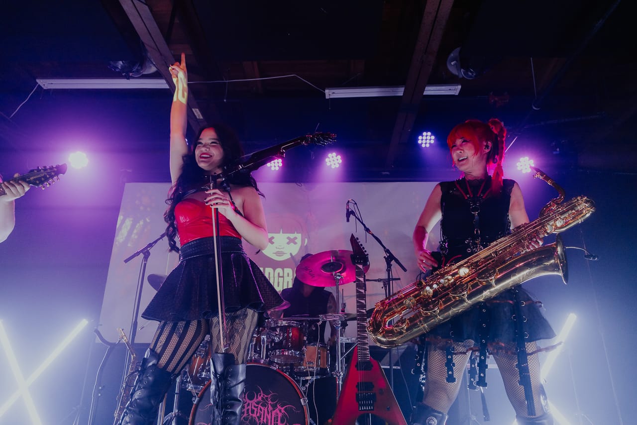 Mia Asano raises her bow overhead as Grace Kelly plays baritone saxophone beside her on stage at the Urban Lounge, Salt Lake City