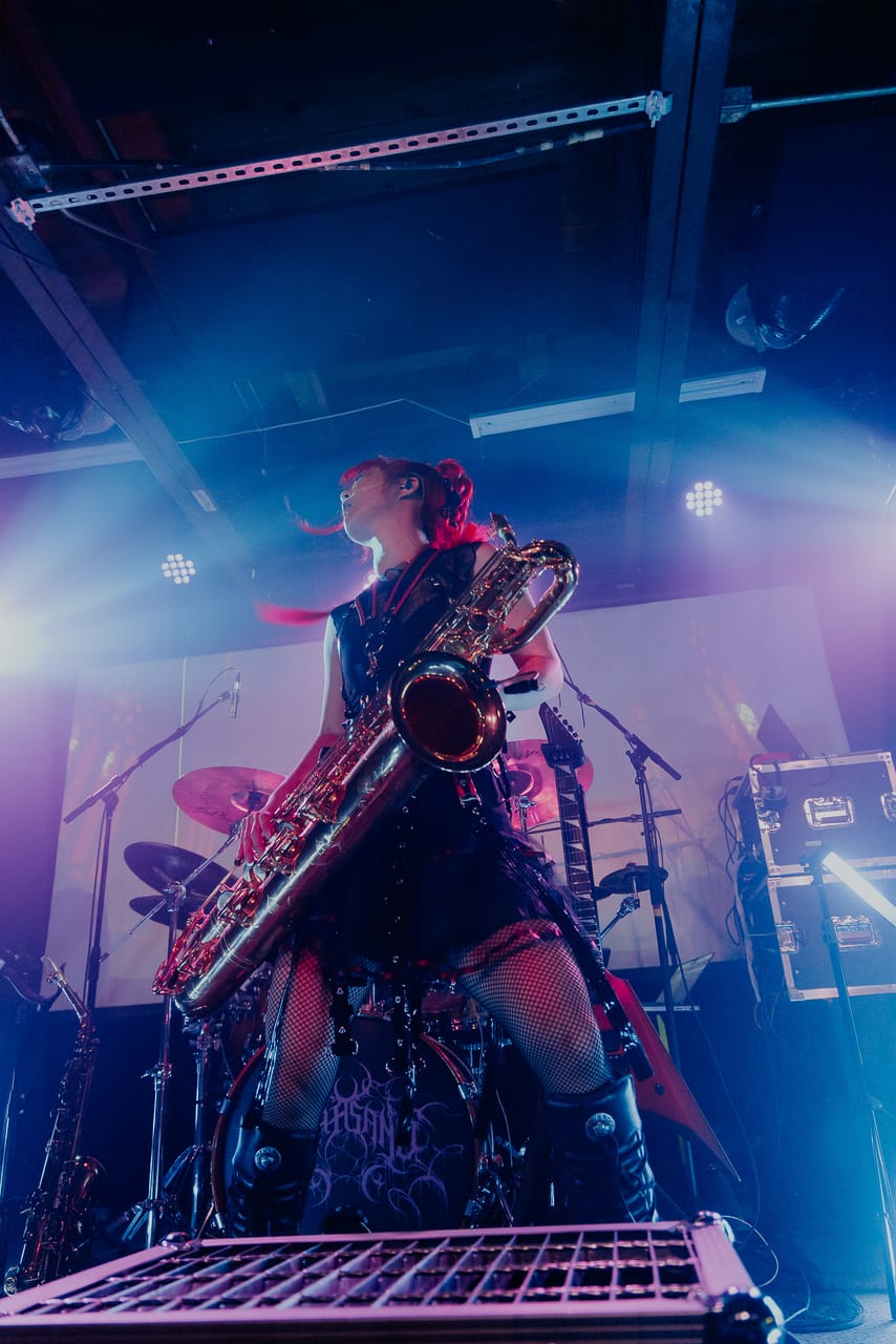 Grace Kelly plays a baritone saxophone from the edge of the stage, shot from below in blue and pink light at the Urban Lounge, Salt Lake City