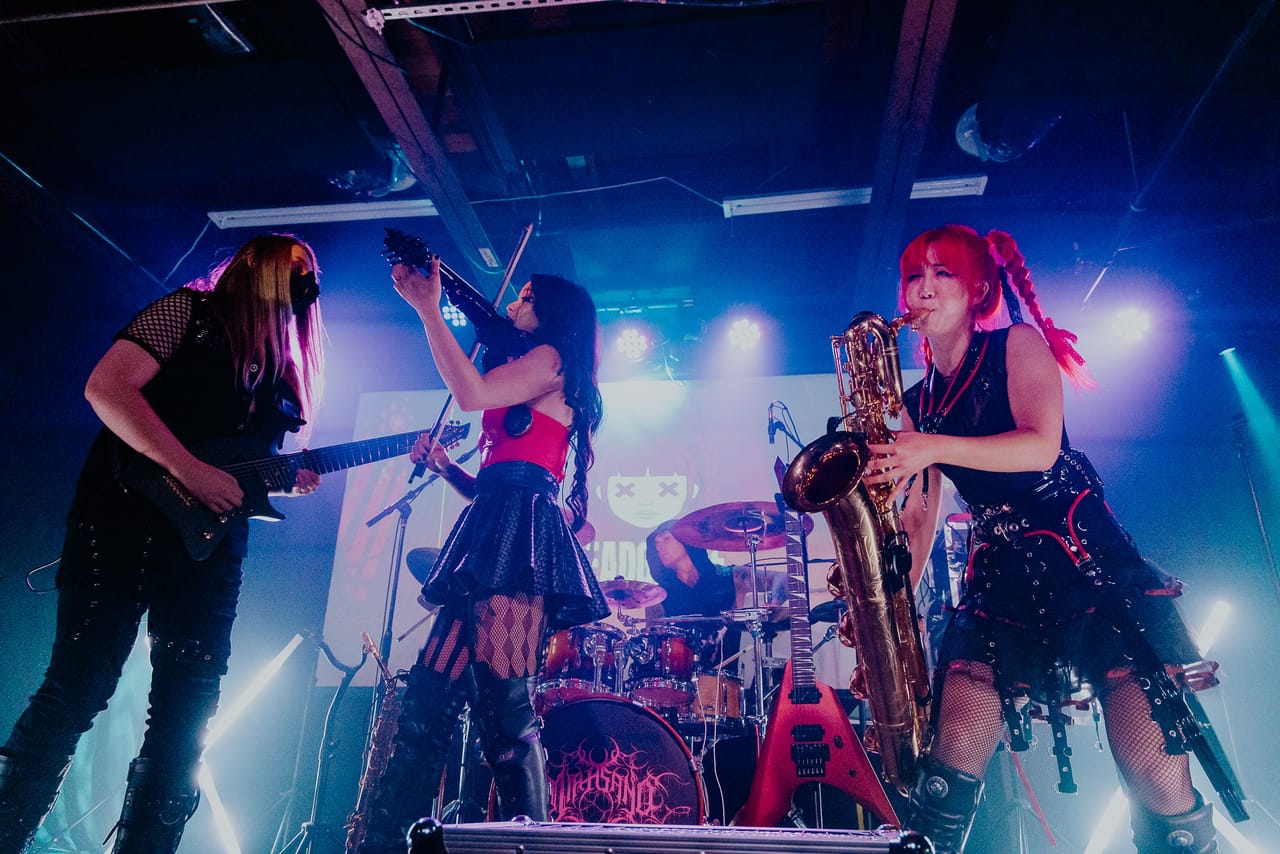 Sam Fairless on guitar, Mia Asano on violin and Grace Kelly on saxophone play together under blue light at the Urban Lounge in Salt Lake City