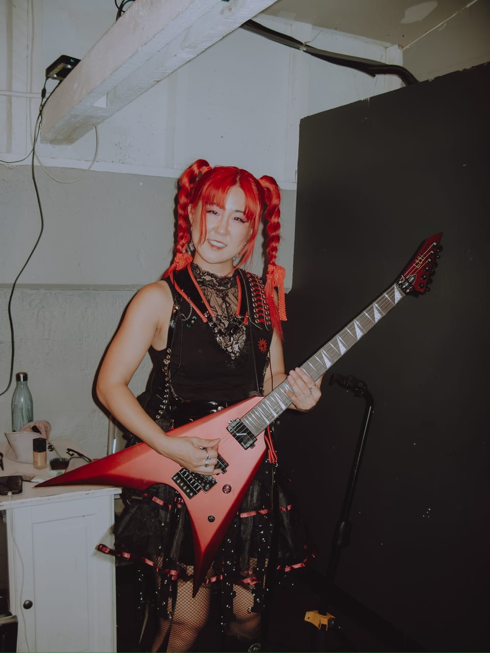 Grace Kelly backstage at The Ritz, smiling and holding her red flying-V guitar