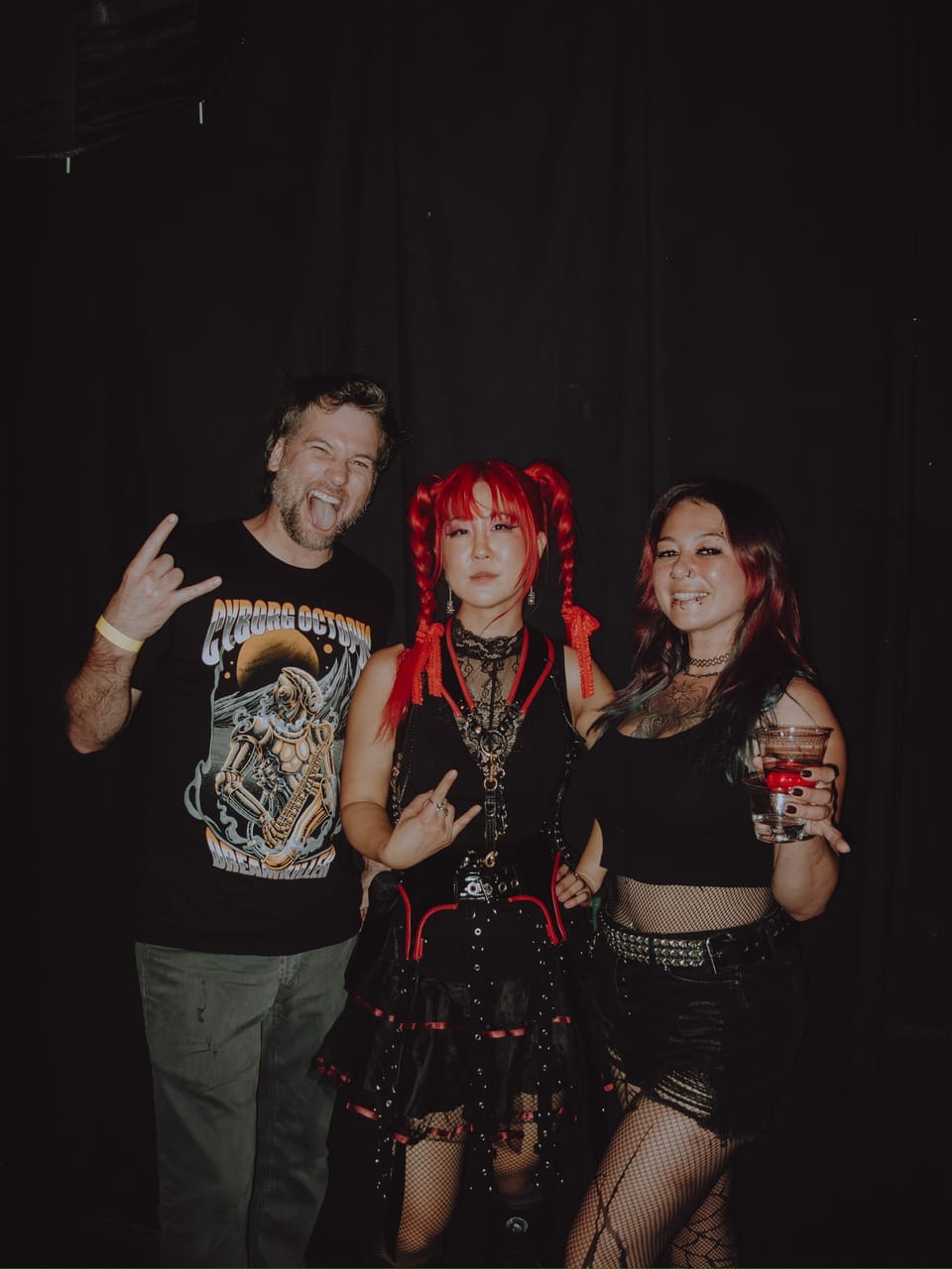 Grace Kelly posing with two fans at The Ritz in San Jose, one throwing horns in a Cyborg Octopus shirt and the other holding a drink