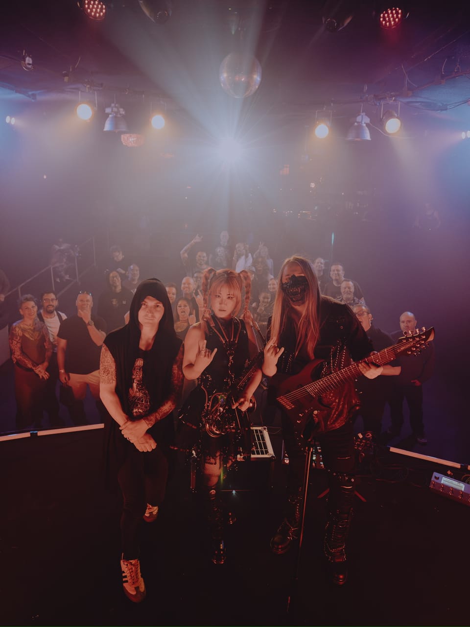 DEADGRACE on The Ritz stage — drummer Kyle Brian in a hood, Grace Kelly throwing horns, and masked guitarist Sam Fairless holding an 8-string guitar — with the San Jose crowd throwing horns behind them under a mirror ball