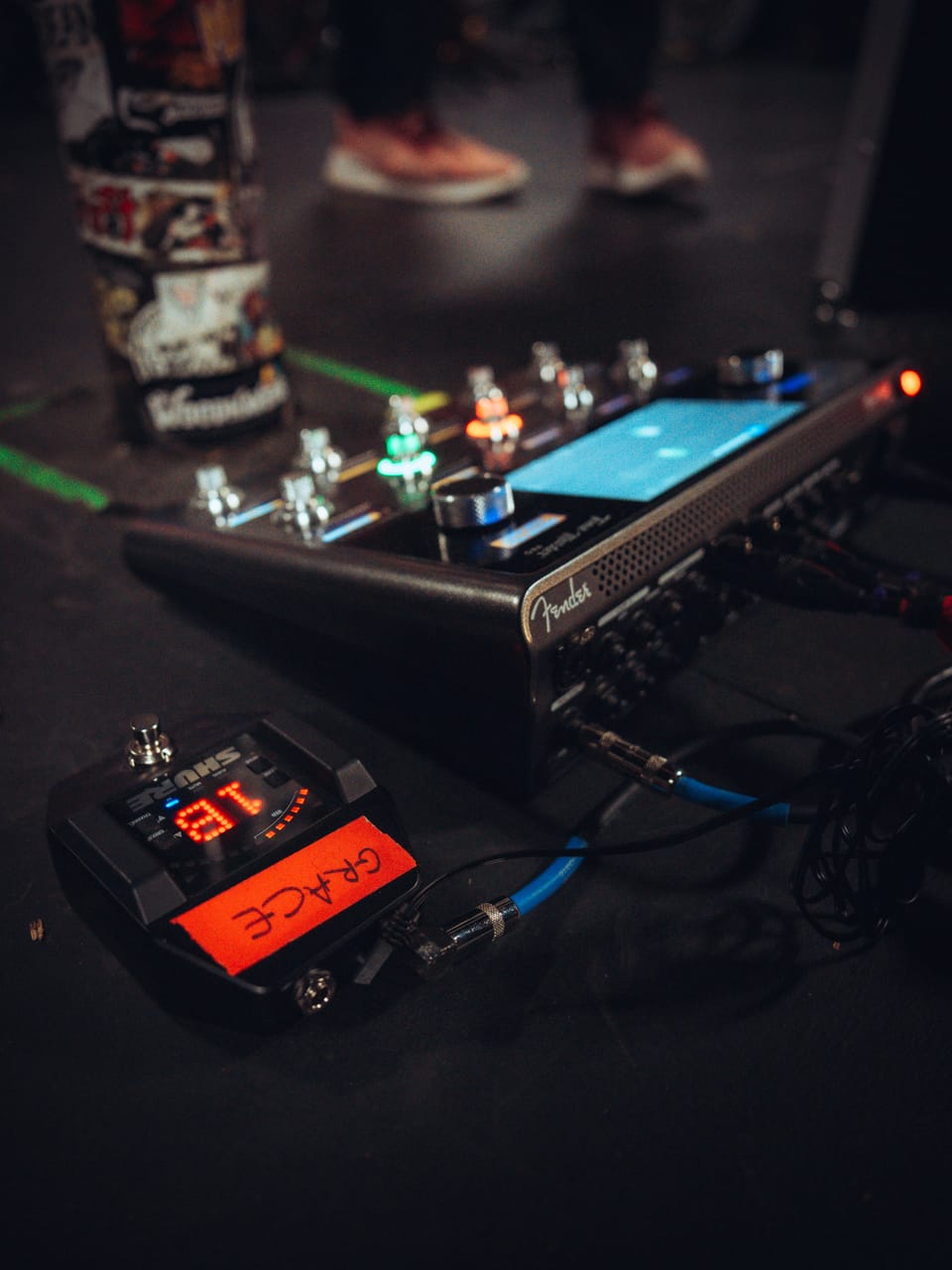 Grace Kelly's pedalboard on the stage floor at El Corazon: a Fender multi-effects unit with a lit screen and a tuner pedal labeled GRACE