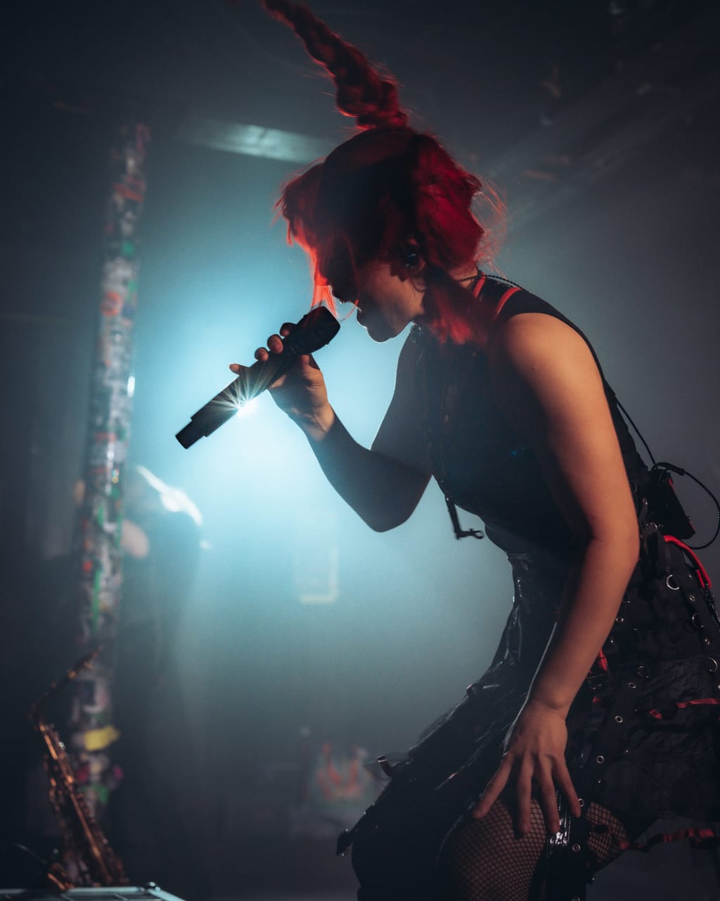 Grace Kelly crouches and sings into a microphone, a braid flying above her head, backlit by a teal spotlight at El Corazon in Seattle