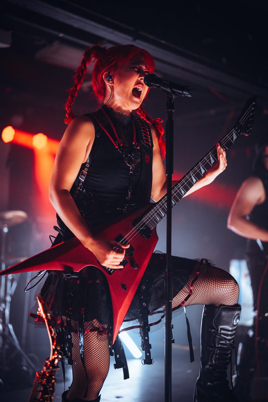 Grace Kelly of DEADGRACE sings at a microphone stand while playing a red flying-V guitar under red light at El Corazon, Seattle