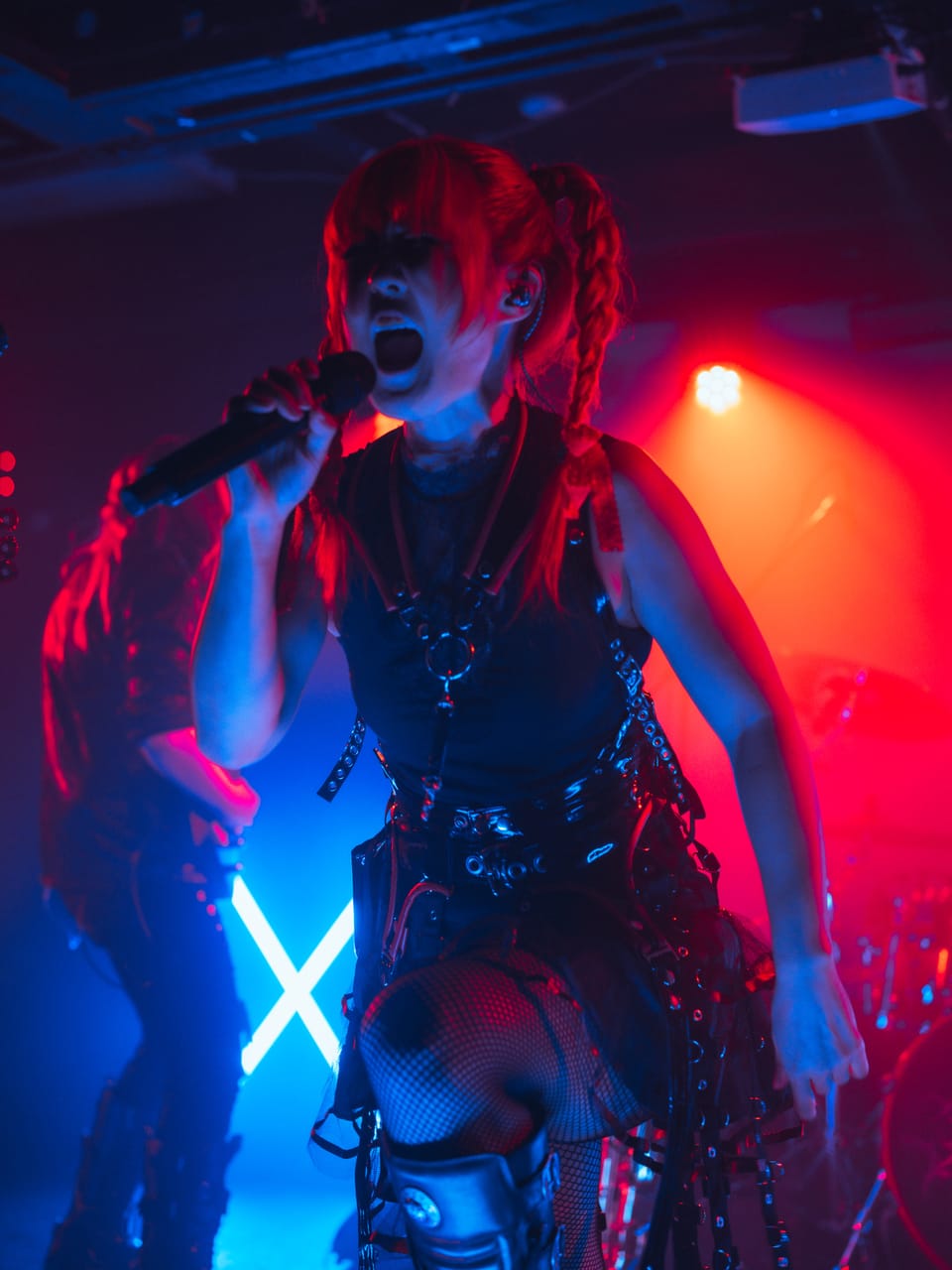 Grace Kelly screams into a handheld microphone, one knee raised, under red and blue light with a neon X behind her at El Corazon in Seattle