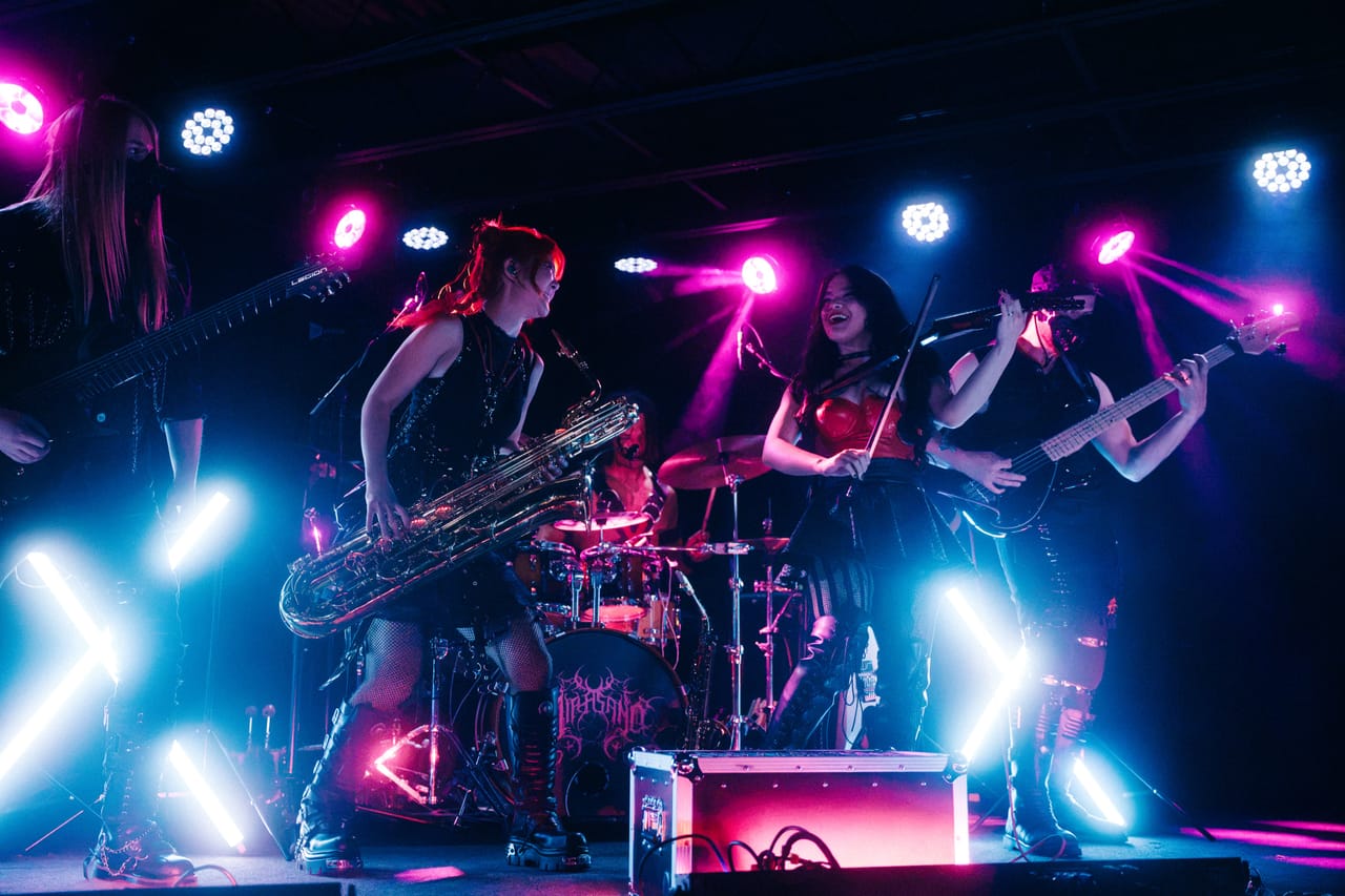 Sam Fairless on guitar, Grace Kelly on a big low saxophone, Mia Asano on violin and Hampus Isaksson on bass play together under pink and blue lights at The District in Spokane